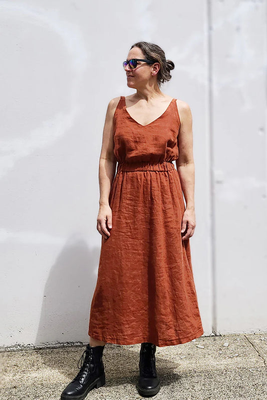 Woman wearing a rust-colored dress standing against a white wall.
