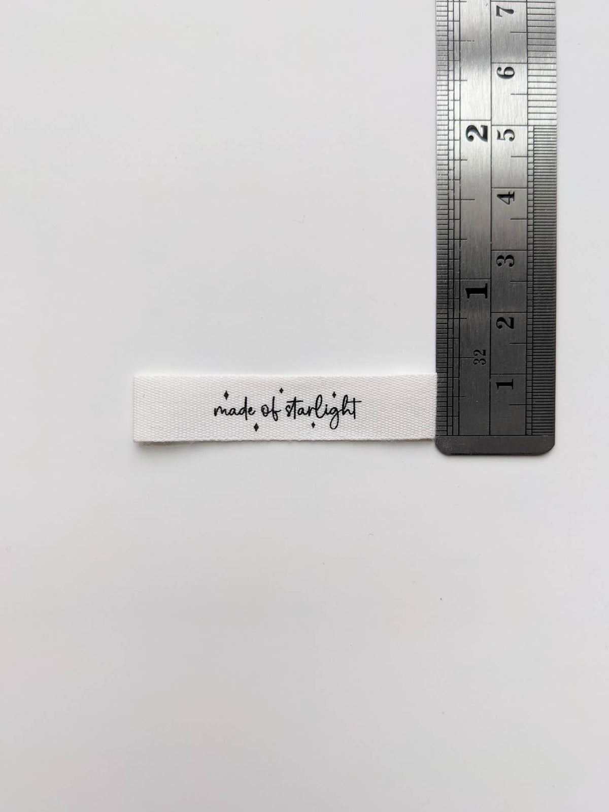 A white fabric label with black script reading 'made of starlight' placed next to a metal ruler on a plain white background.