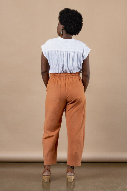 Person wearing a white top and orange pants against a beige background