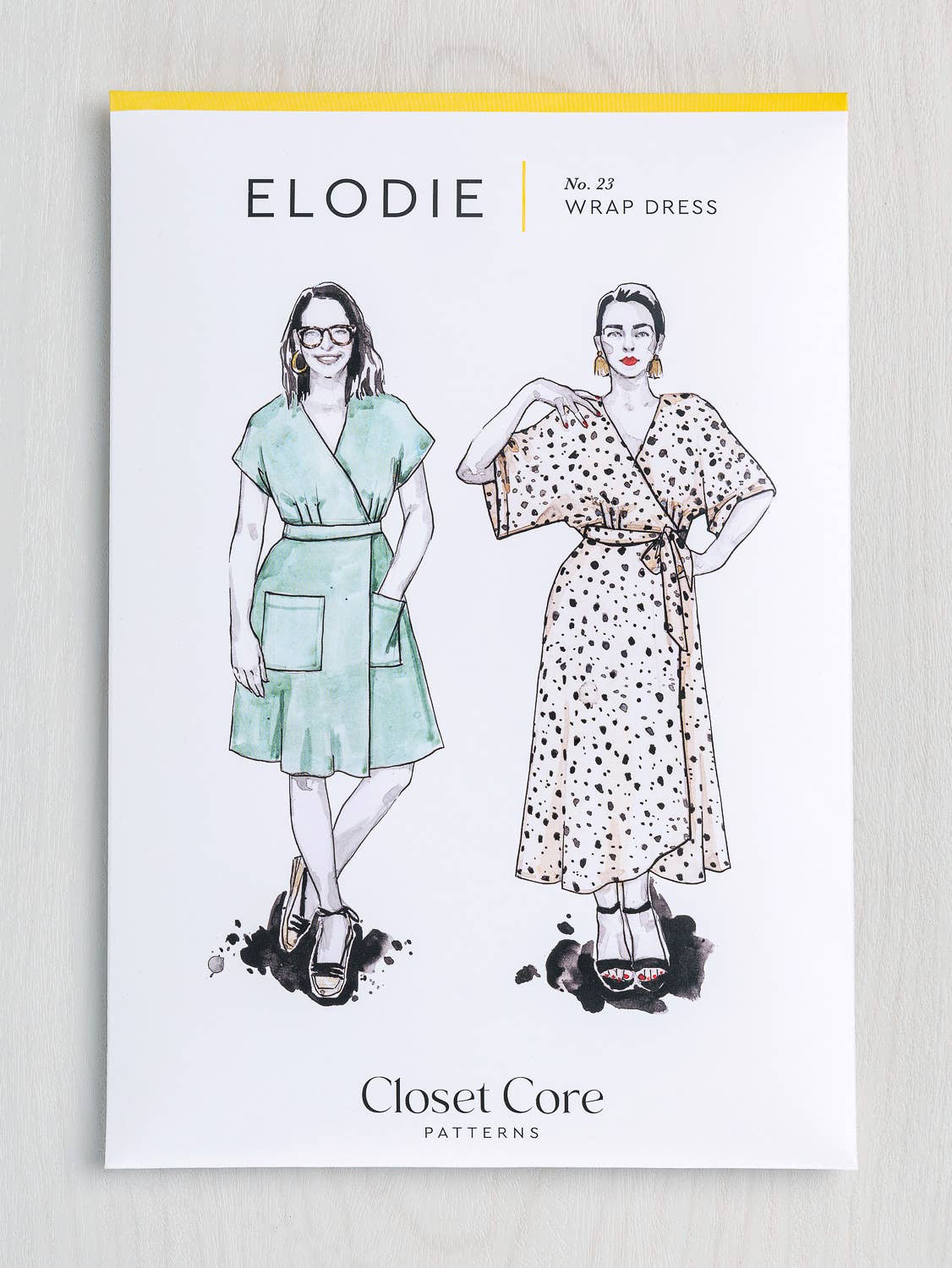 Elodie wrap dress pattern packaging with illustrations of two women wearing dresses, on a light gray background.