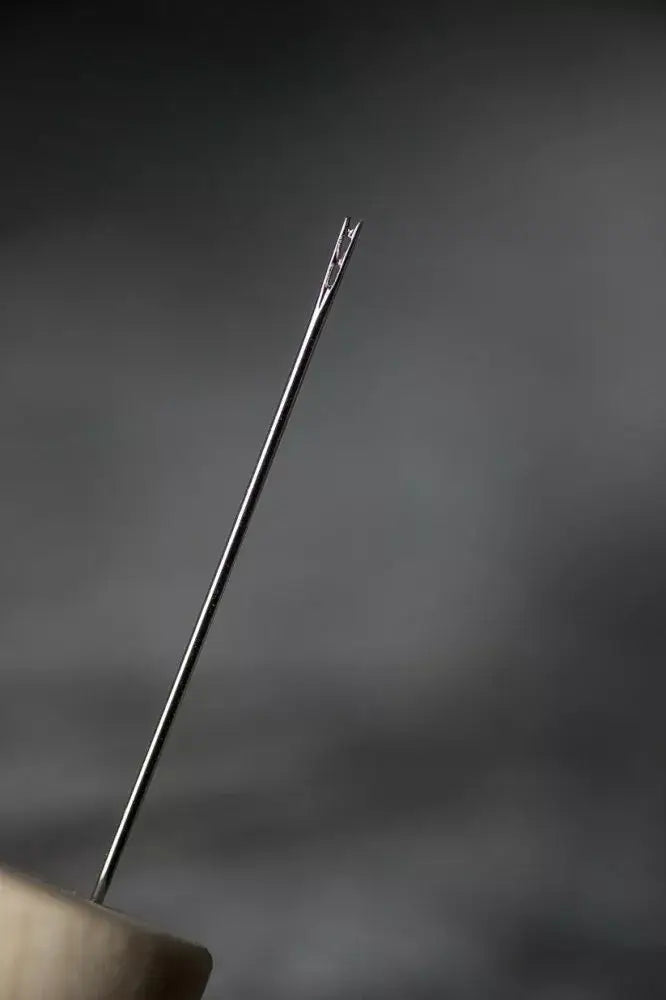 Close-up of a needle held by a hand against a dark background