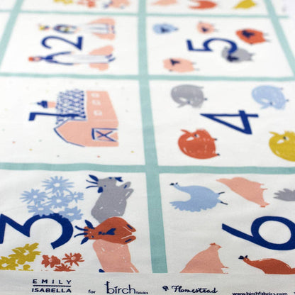 A close-up of a printed fabric or textile panel with a six-panel grid, each containing a large blue number and a small illustrated animal or object in pastel colors. The bottom edge shows the text 'EMILY ISABELLA for birch houses' and a website, indicating the product brand.