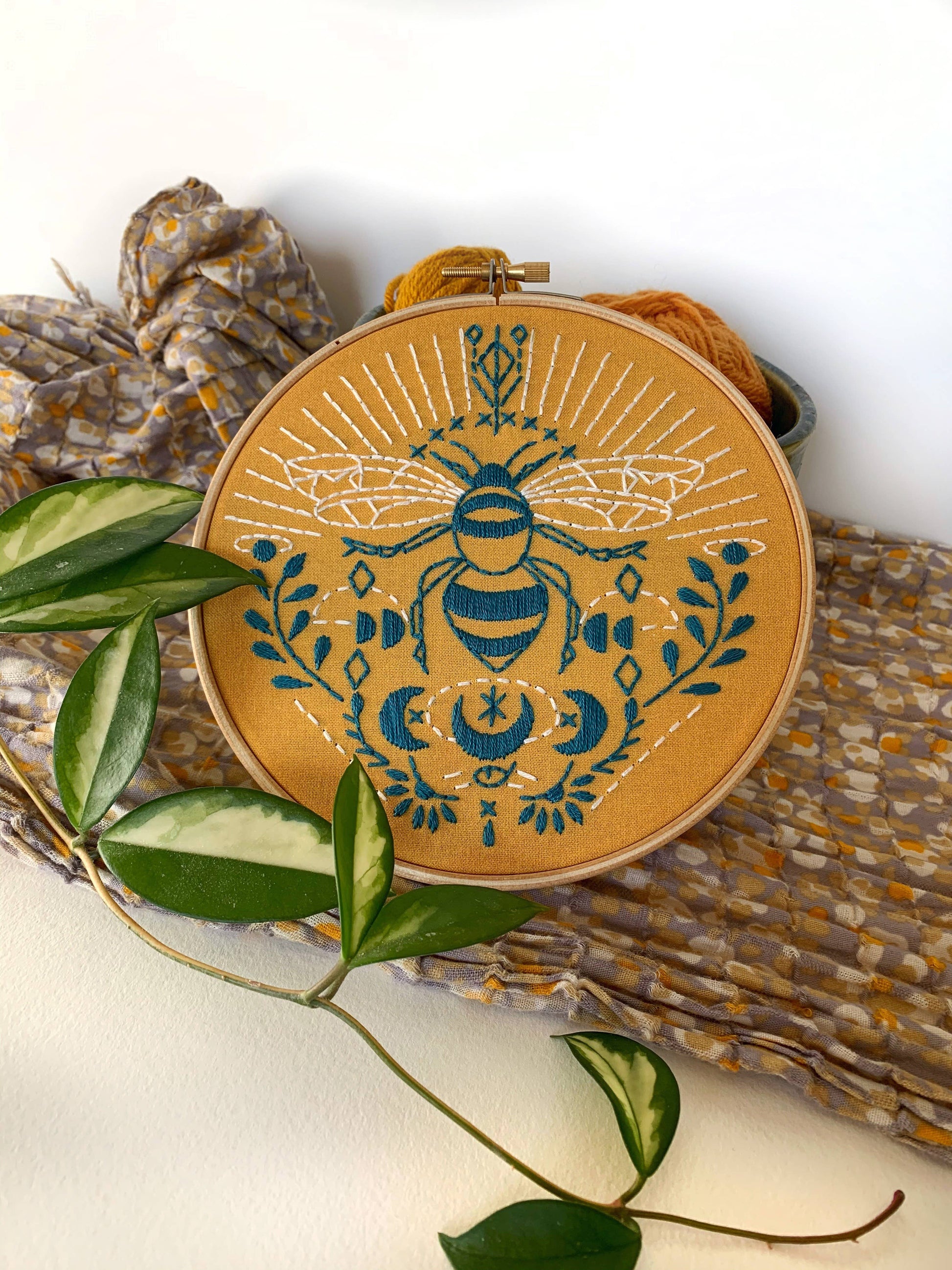 Embroidery hoop with bee design on a woven mat with leaves