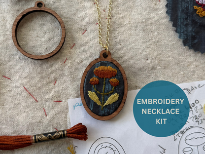 Embroidery necklace kit with wooden pendant, thread, and fabric on a textured surface.