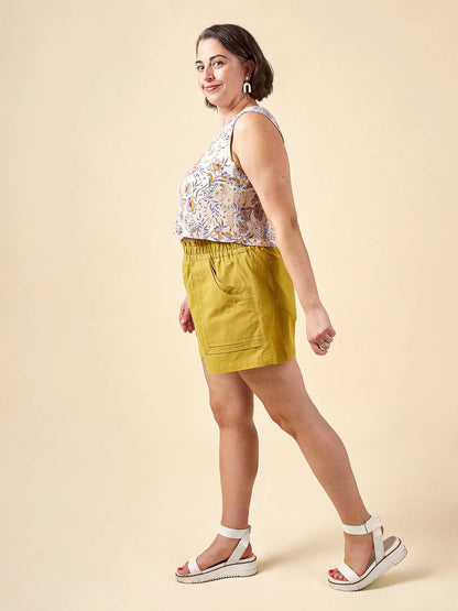 Woman wearing a floral top and yellow shorts on a beige background