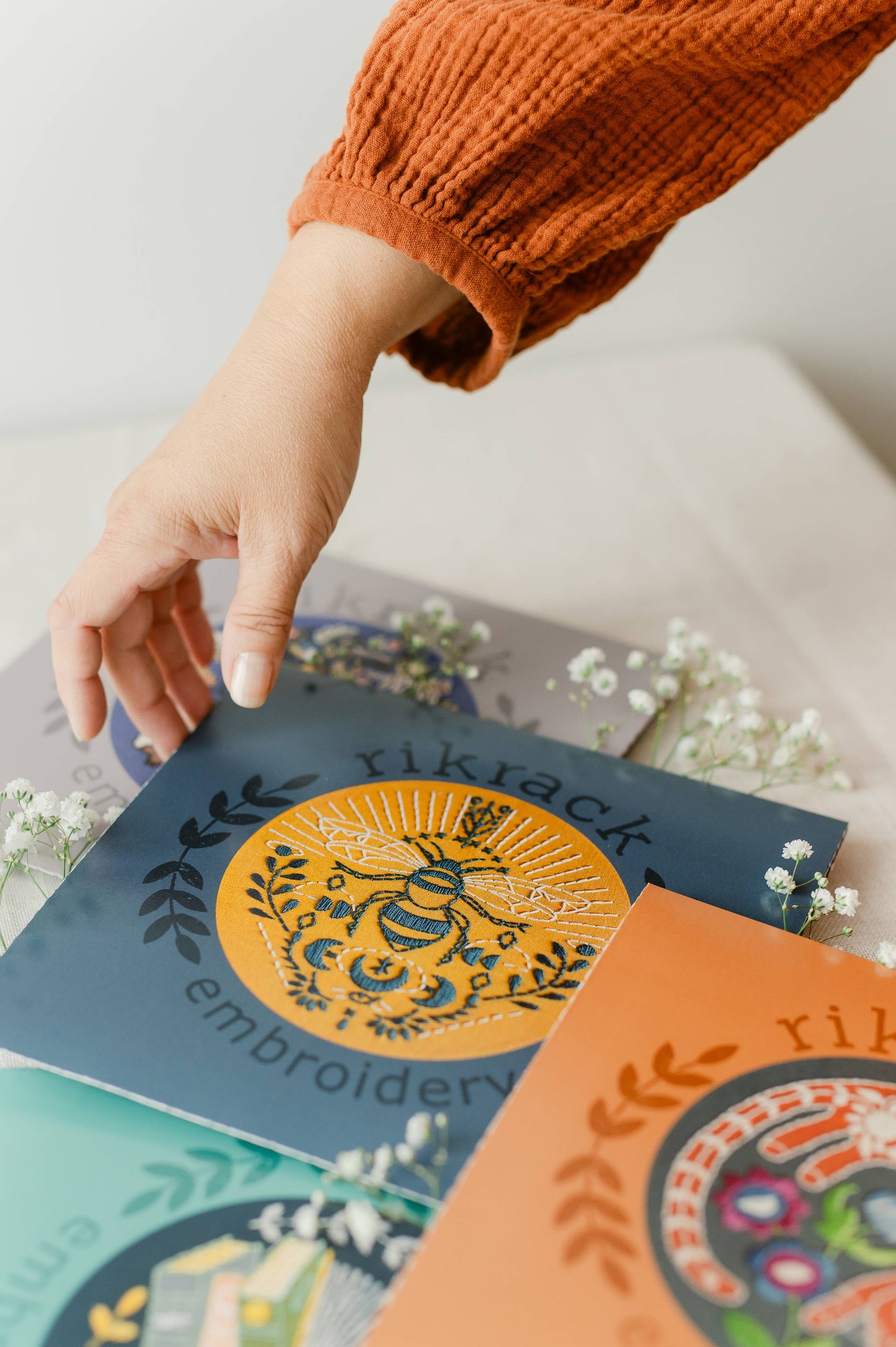 Hand holding a book with embroidery designs on a light background