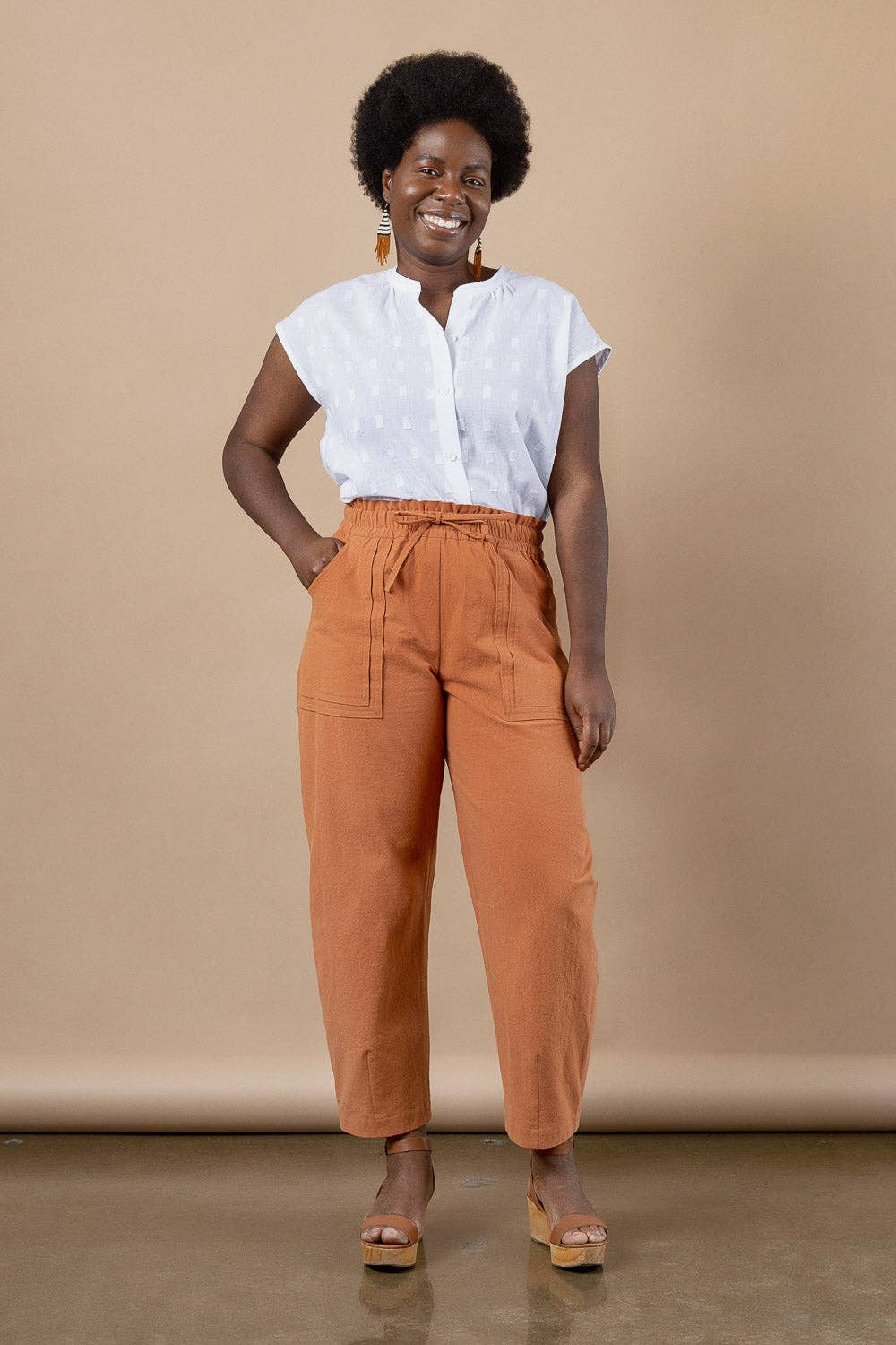 Woman wearing a white blouse and orange pants against a beige background