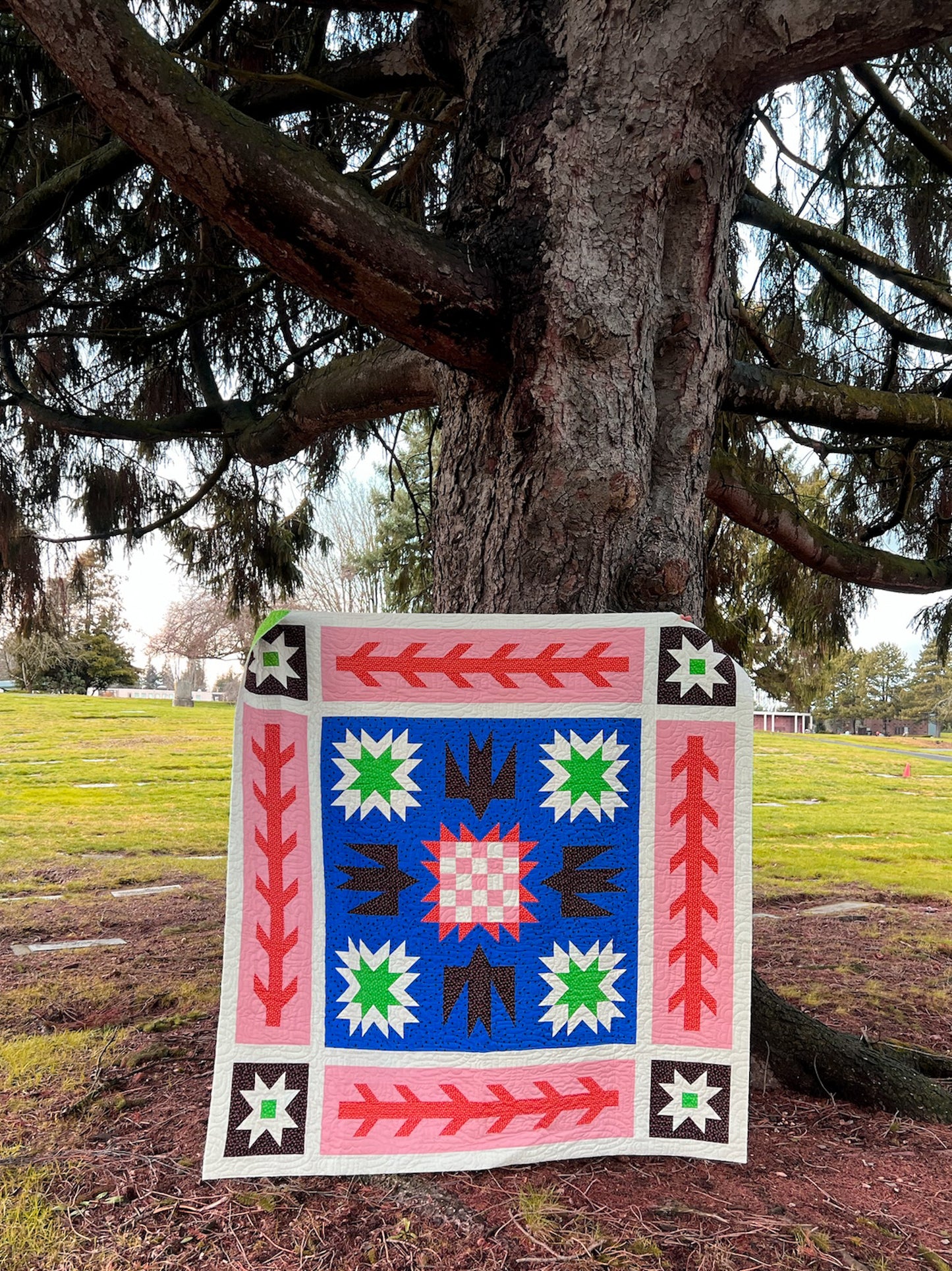 Colorful quilt with geometric patterns displayed outdoors against a tree