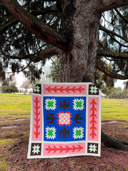 Colorful quilt with geometric patterns displayed outdoors against a tree