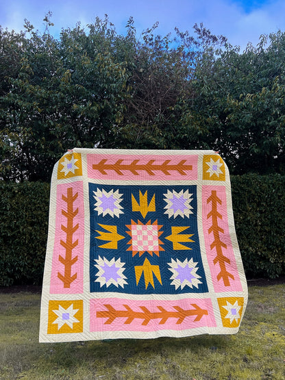 Colorful quilt with geometric patterns on a grassy area with trees in the background