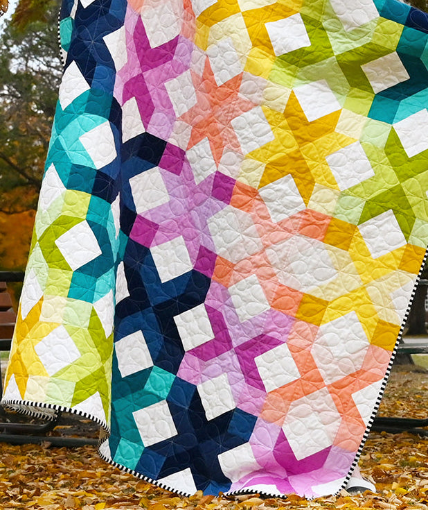 The quilt features a colorful geometric star and diamond pattern in pink, purple, blue, green, yellow, and white.