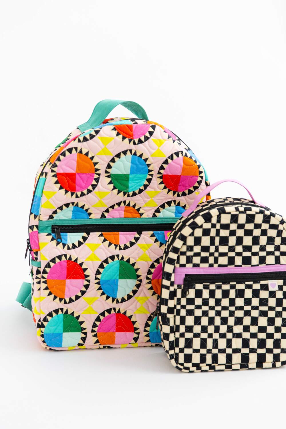 Two backpacks, large one (Archie) with a colorful geometric pattern and the small one (Violet) with a black and white checkered pattern, on a white background.