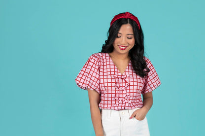 Woman wearing a red checkered top and white pants against a blue background