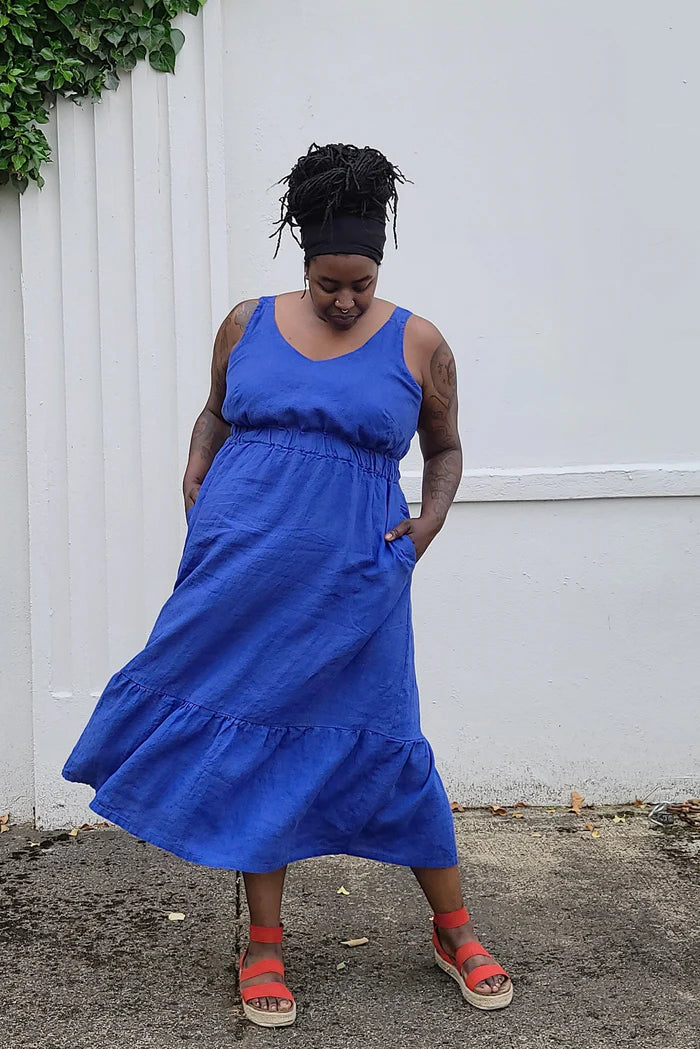 Woman wearing a blue dress standing against a white wall.