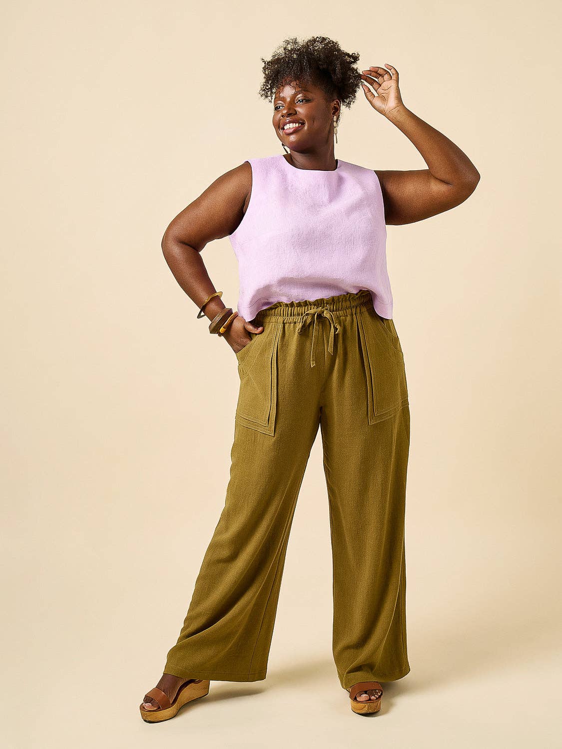 Woman wearing a light purple sleeveless top and olive green wide-leg pants on a beige background